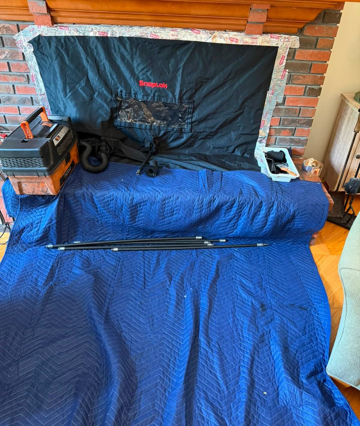 Fireplace opening sealed with a taped containment sheet and a HEPA vacuum running, with quilted blankets covering the hearth and floor before a chimney sweep