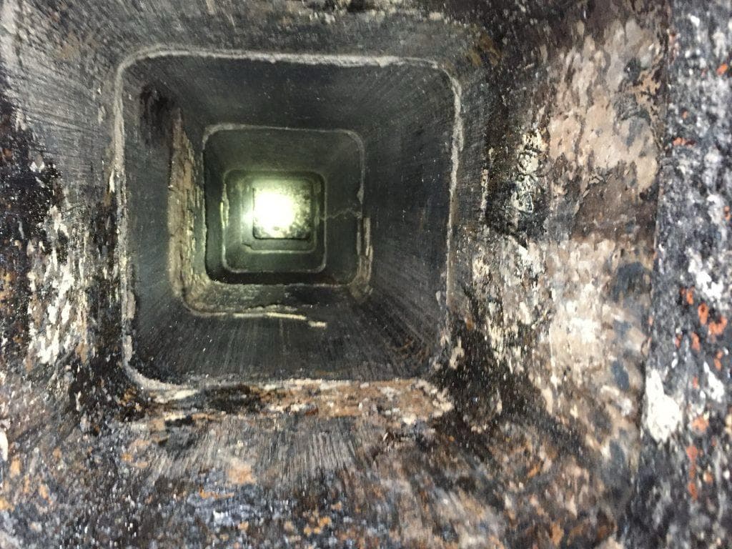 View straight down a clay tile flue showing heavy creosote and soot buildup on the walls
