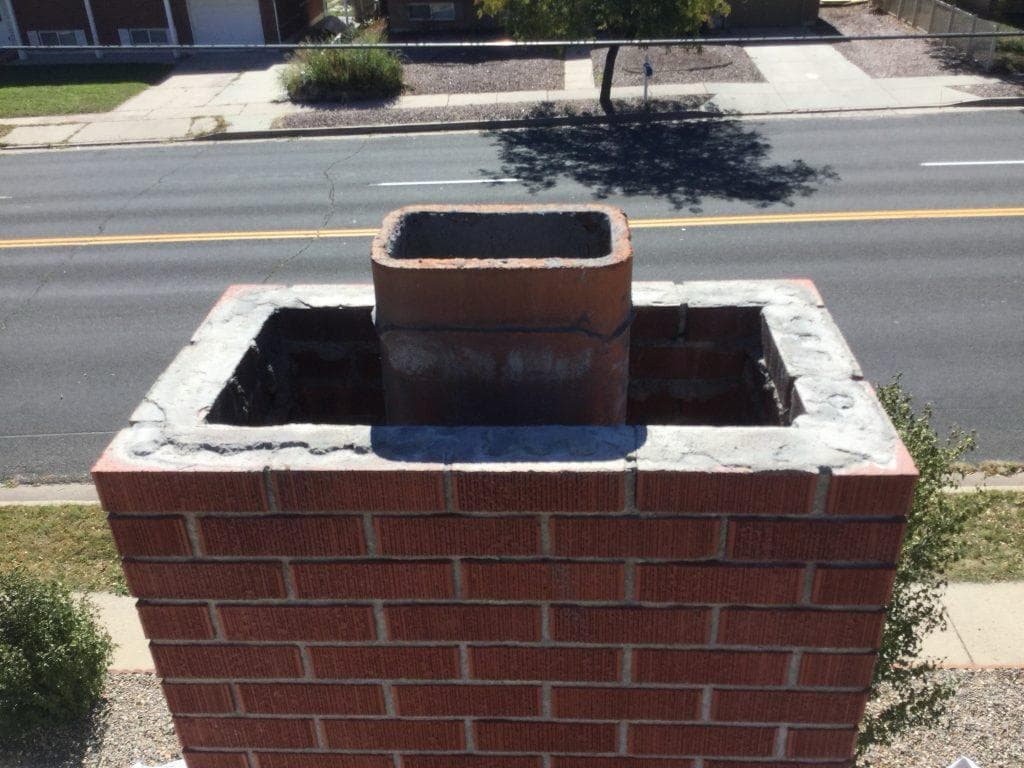 Top of a brick chimney with two flues and a cracked, patched mortar crown