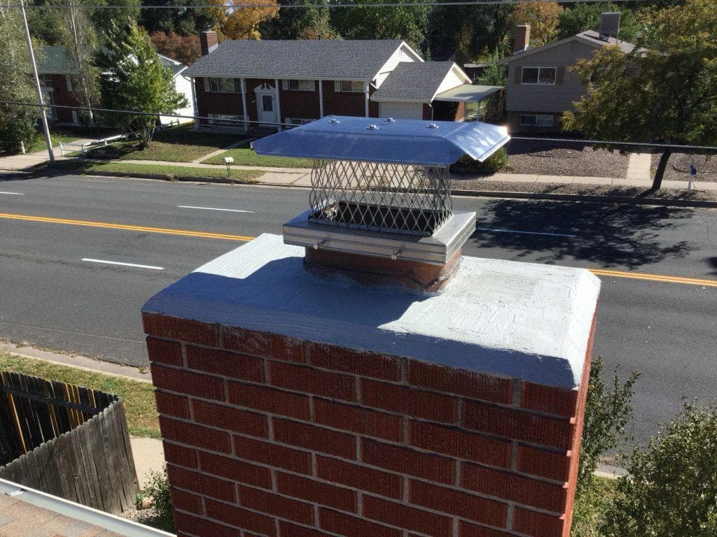 Newly installed stainless steel chimney cap on a red brick chimney with a freshly sealed crown