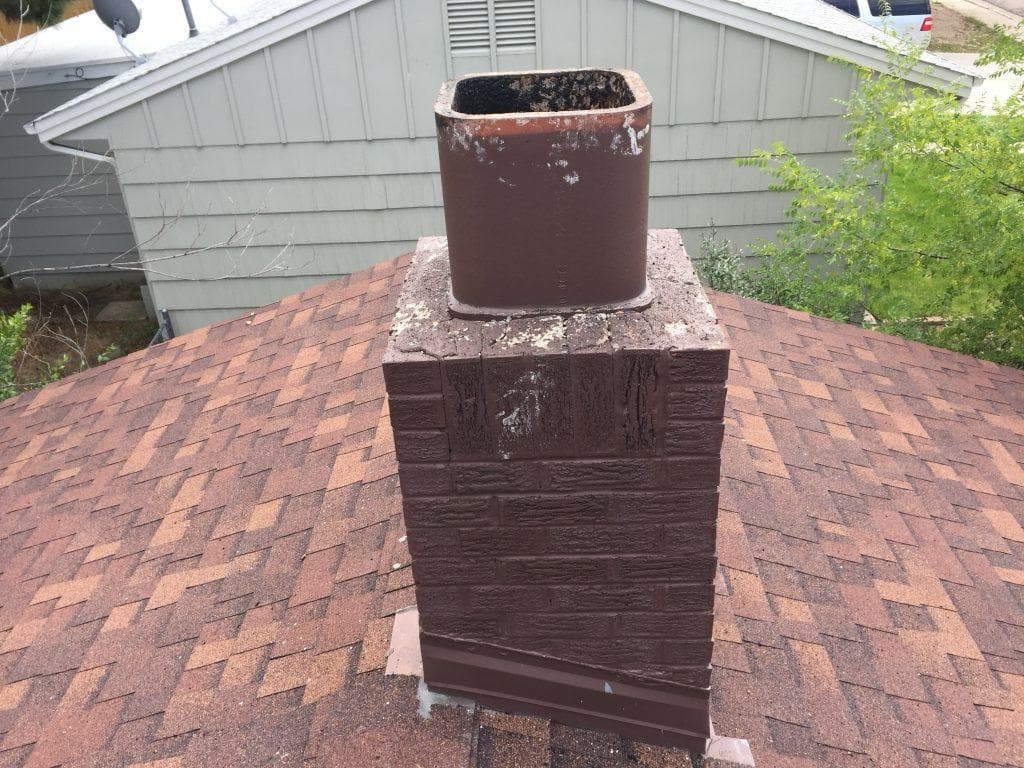 Open uncapped clay flue tile on a painted brick chimney, exposed to rain and animals