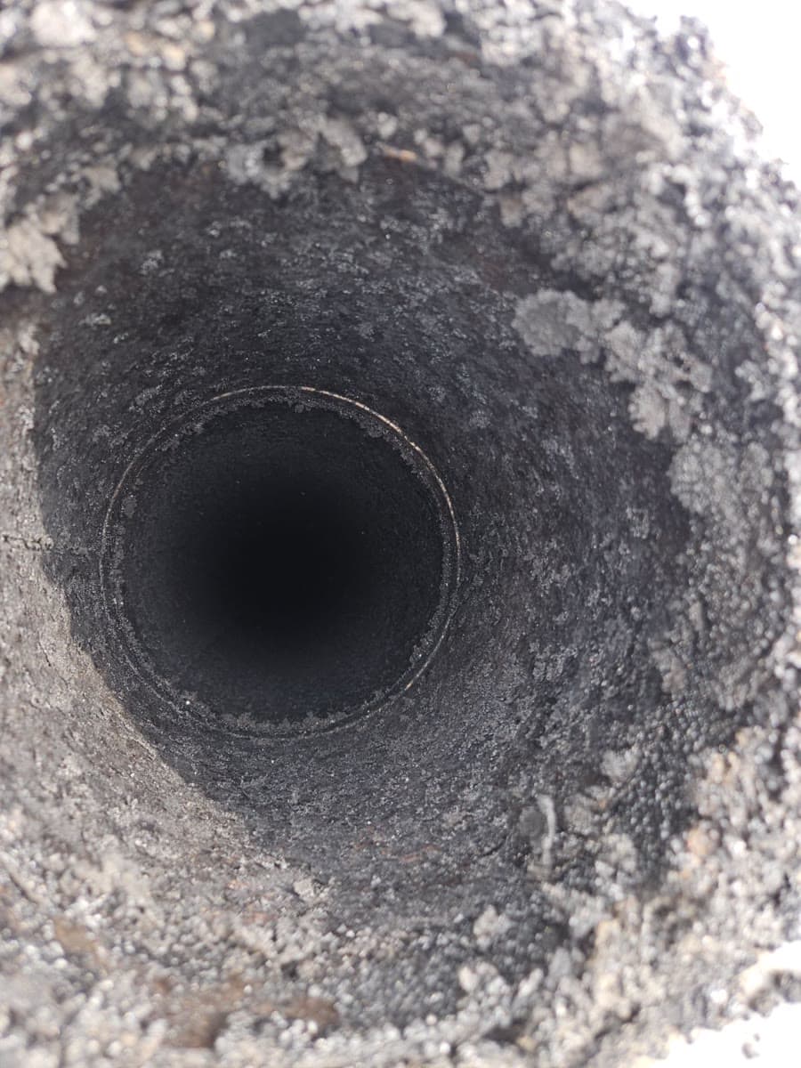 Looking down a round metal flue liner coated in thick flaky creosote and soot before sweeping