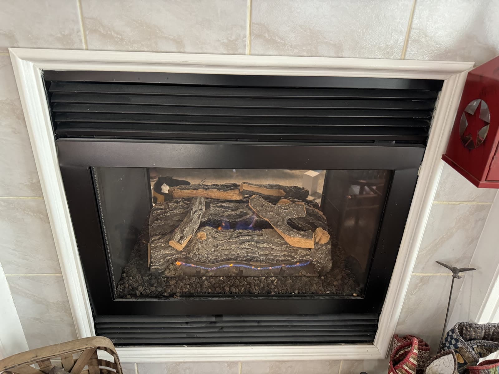 Direct-vent gas fireplace running behind fixed glass, set into a tiled wall with a white timber surround