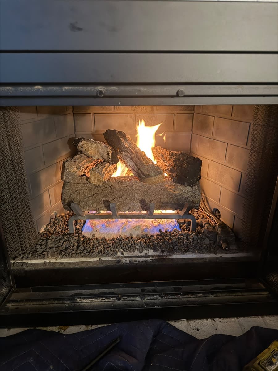 The same gas fireplace after service, logs reset and burning with a clean blue base flame